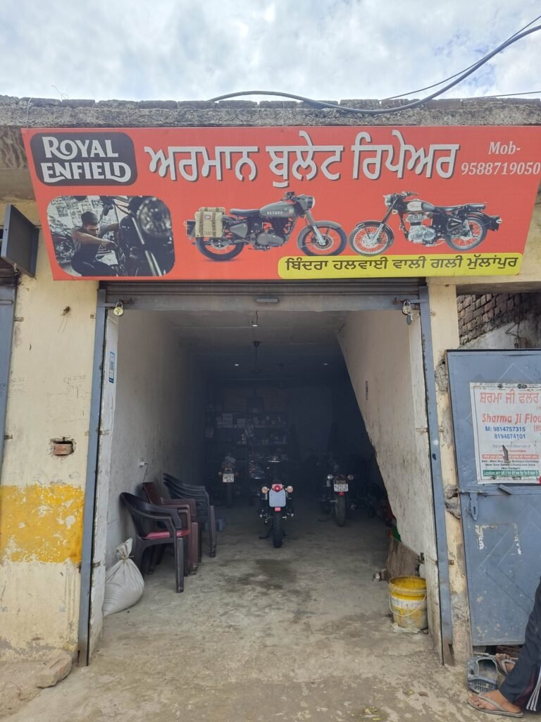 Red shop sign advertising Royal Enfield in Punjabi above a garage entrance with motorcycles inside the workshop.