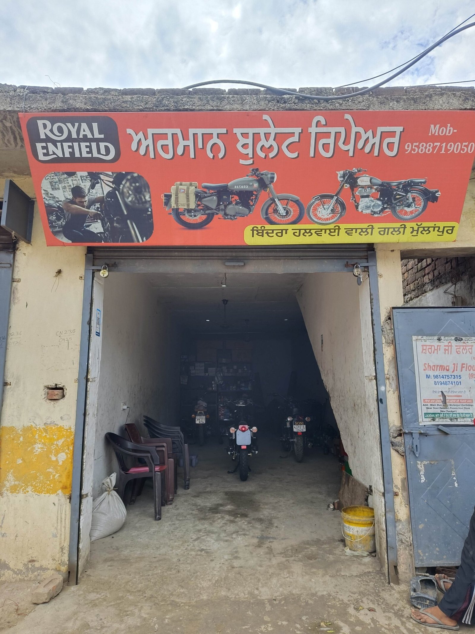 Red shop sign advertising Royal Enfield in Punjabi above a garage entrance with motorcycles inside the workshop.