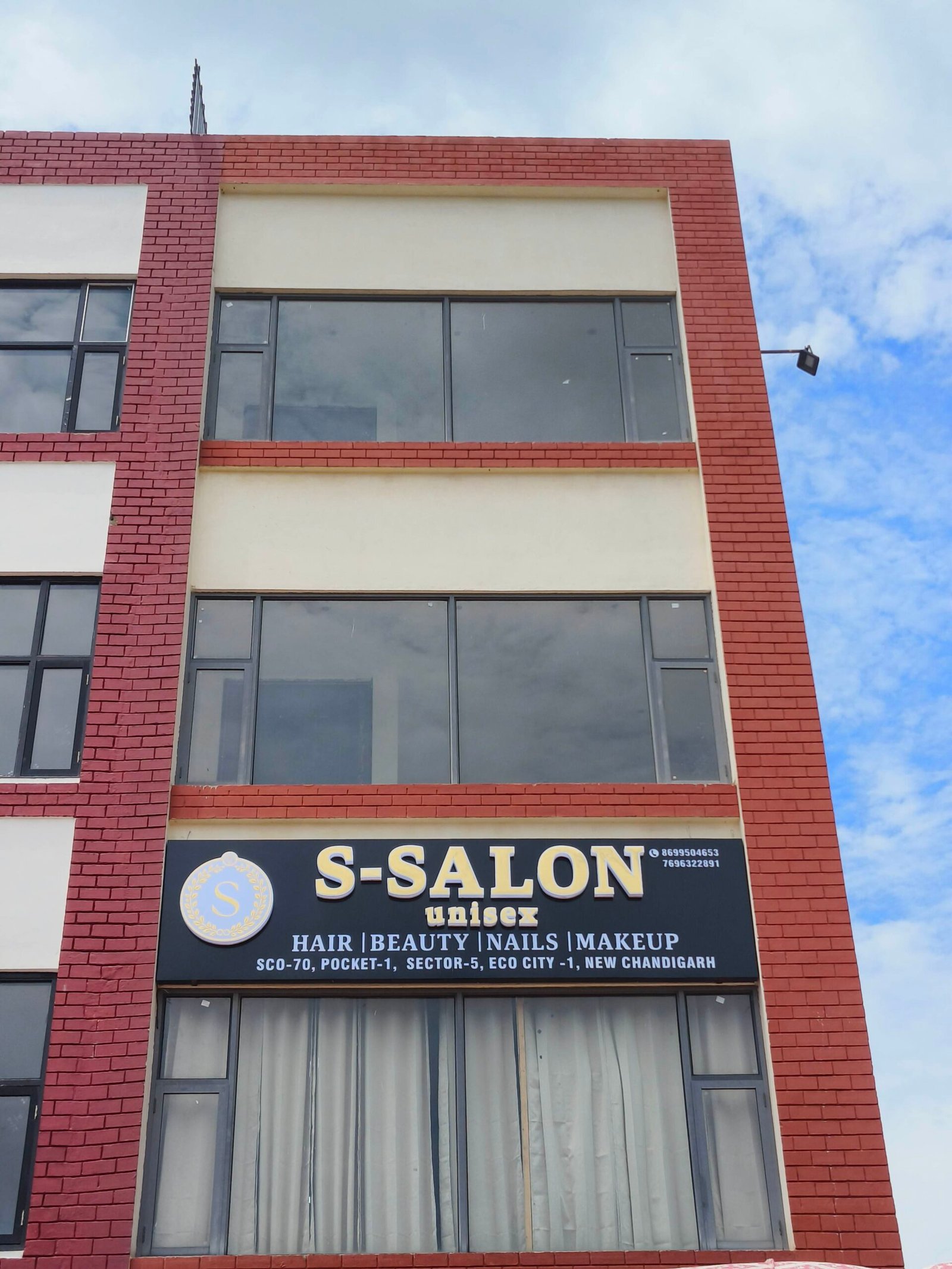 Front of a red brick building with large glass windows and a 'S-SALON unisex' salon sign against a blue sky.