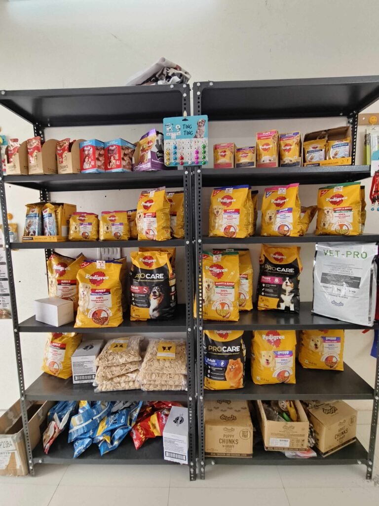Metal shelving unit filled with bags of dog food and treats (Pedigree and other brands) on multiple shelves in a pet store.