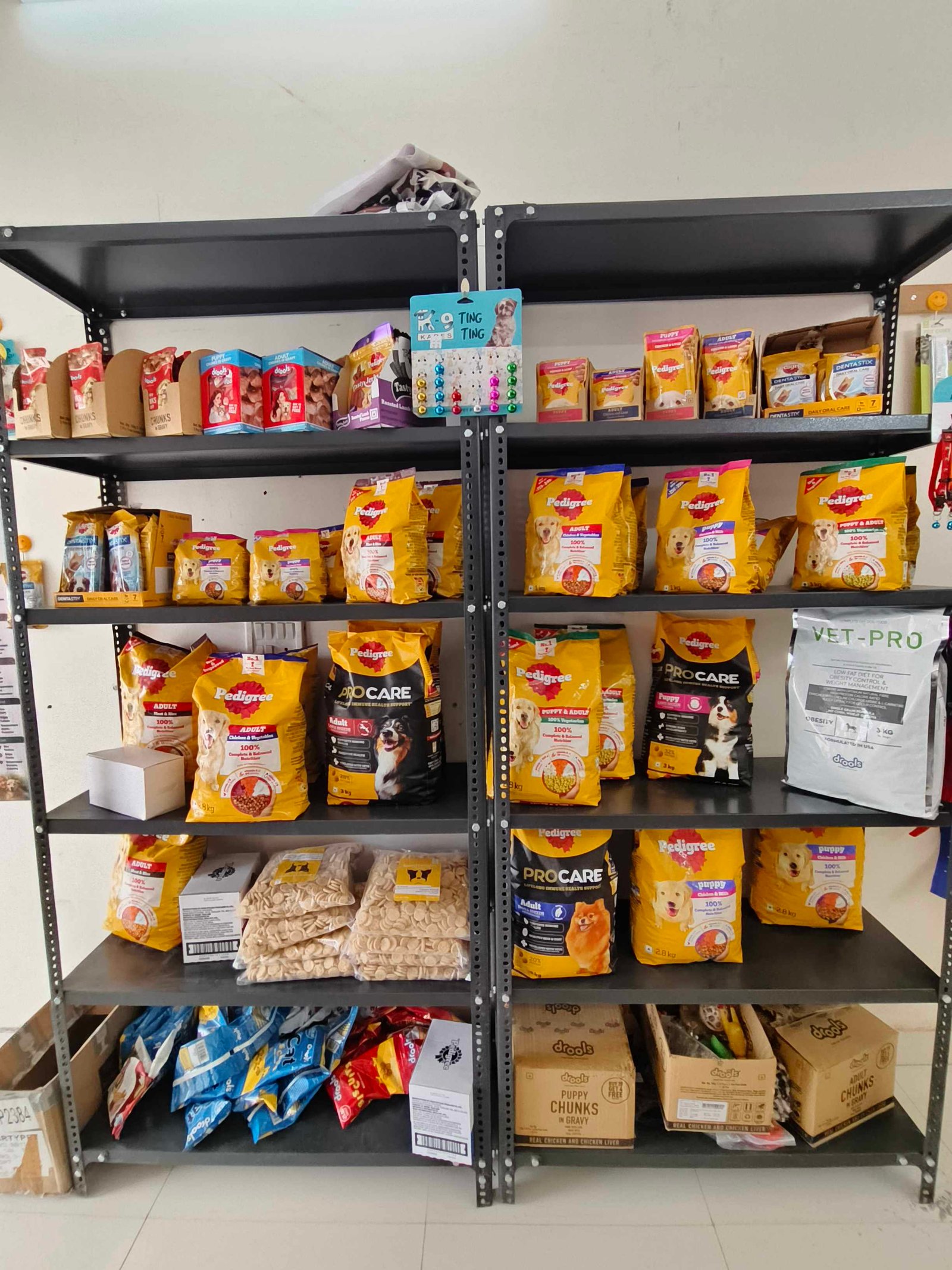 Metal shelving unit filled with bags of dog food and treats (Pedigree and other brands) on multiple shelves in a pet store.