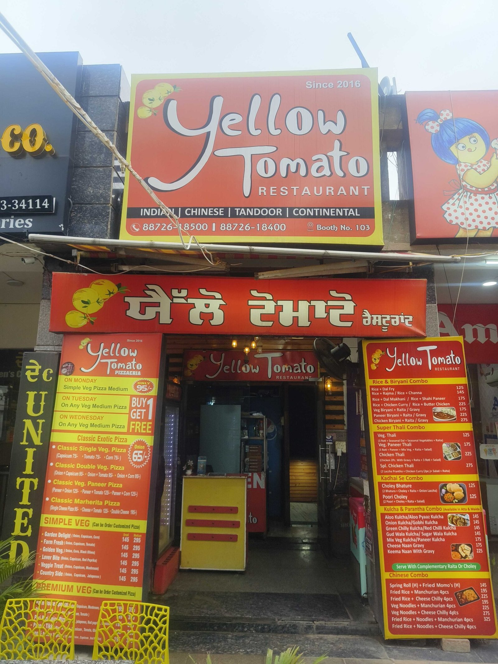Front of Yellow Tomato Restaurant with a large orange sign reading 'Yellow Tomato Restaurant' and smaller menu boards outside, indicating Indian/Chinese cuisine.